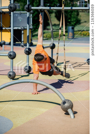 Outdoor TRX Core Workout. Muscular man in sportswear training outdoors, doing challenging trx side plank, using park equipment and straps Outdoor TRX Core Workout. Muscular man in sportswear training outdoors, doing challenging trx side plank, using park equipment and straps 116366089