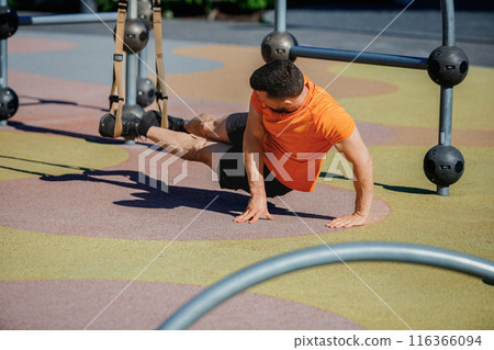 Athletic man sportswear placing feet on trx straps, doing plank exercises, growing strength. Outdoor trx workout Athletic man sportswear placing feet on trx straps, doing plank exercises, growing strength. Outdoor trx workout 116366094