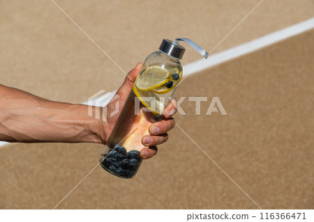 Reusable sport glass bottle with lemon and berry or isotonic in athlete hand. Concept detox, drinking water. Daily water tracker. Water balance for workout. 116366471