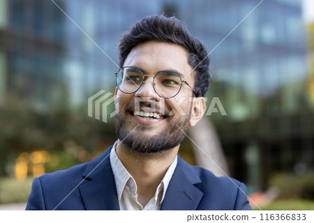 Smiling young professional wearing glasses in business attire. Outdoor portrait taken in urban business district. Perfect for career, corporate, and business themes. Smiling young professional wearing glasses in business attire. Outdoor portrait taken in urban business district. Perfect for career, corporate, and business themes. 116366833