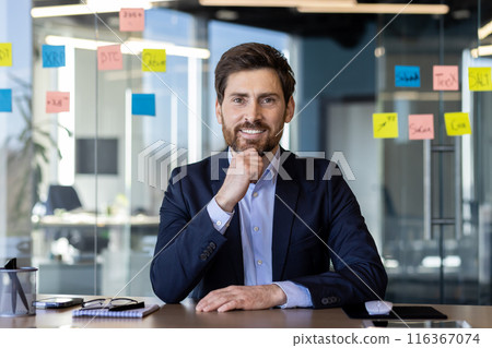 A professional Caucasian businessman with a beard poses confidently in a contemporary office environment, surrounded by glass walls and sticky notes. A professional Caucasian businessman with a beard poses confidently in a contemporary office environment, surrounded by glass walls and sticky notes. 116367074