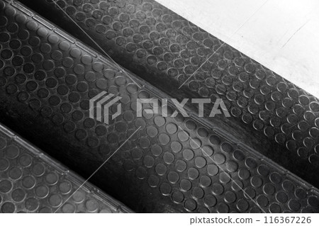 Black rubber mat with a non-slip pattern covers an industrial stairway Black rubber mat with a non-slip pattern covers an industrial stairway 116367226