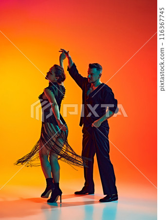 Gentleman and lady, elegant couple dancing bachata, performing with artistry against gradient yellow orange background in neon light Gentleman and lady, elegant couple dancing bachata, performing with artistry against gradient yellow orange background in neon light 116367745