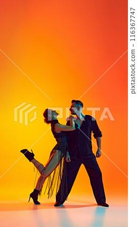 Romantic dance style. Artistic and talented man and woman dancing bachata against gradient yellow orange background in neon light Romantic dance style. Artistic and talented man and woman dancing bachata against gradient yellow orange background in neon light 116367747