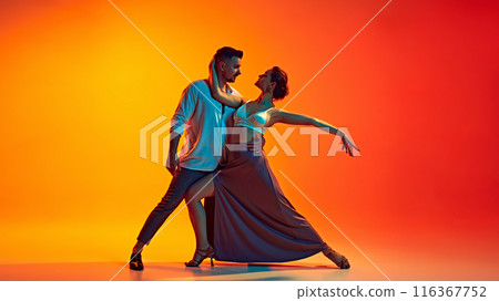 Dynamic dance duo. Romantic and passionate man an woman dancing bachata against gradient yellow orange background in neon light Dynamic dance duo. Romantic and passionate man an woman dancing bachata against gradient yellow orange background in neon light 116367752