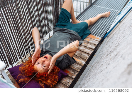 portrait red-haired curly young woman enjoying relaxation on balcony or terrace portrait red-haired curly young woman enjoying relaxation on balcony or terrace 116368092