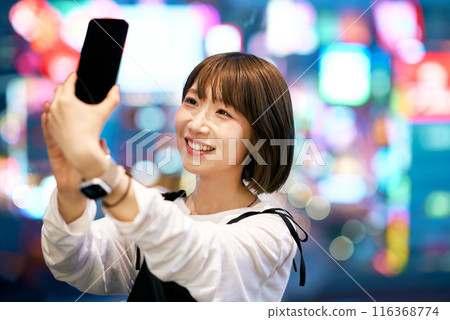 A young woman holding a smartphone in a busy street at night 116368774
