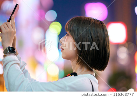 一名年輕女子夜間在市中心舉著智慧型手機 116368777