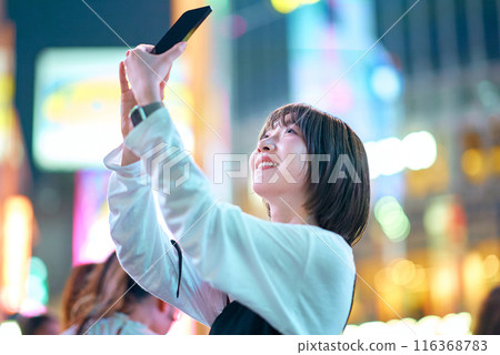 A young woman holding a smartphone in a busy street at night A young woman holding a smartphone in a busy street at night 116368783