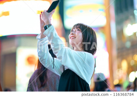 一名年輕女子夜間在市中心舉著智慧型手機 116368784