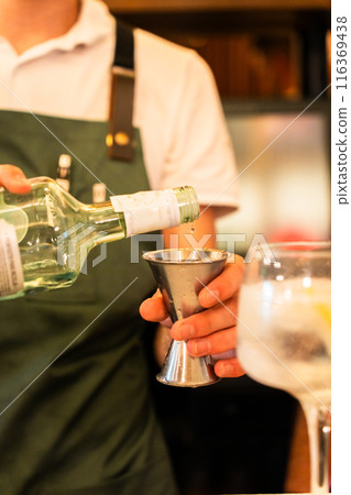 Hands of a bartender measuring the dose of alcohol before preparing the drink. Vertical 116369438