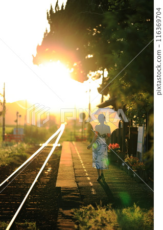 一個帶著陽傘和直線火車線的女人在夏日的夕陽下閃閃發光 116369704