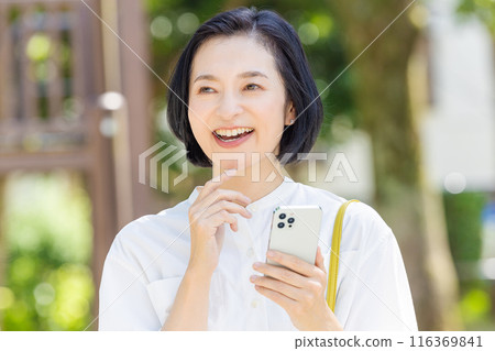 A middle-aged woman looking at her smartphone among the fresh greenery 116369841