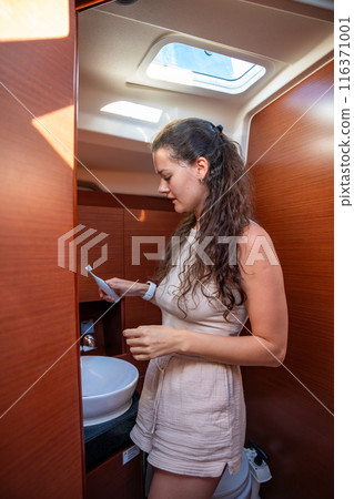 Young Woman brushing her teeth with an electric brush in bathroom of a yacht during sailing in sea. Yacht life concept. Trip around the world 116371001