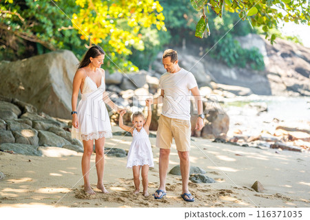 Happy young family of three taking a walk on the beach, having a fun on seashore in the shade of trees and palms. Happy family concept. Happy young family of three taking a walk on the beach, having a fun on seashore in the shade of trees and palms. Happy family concept. 116371035