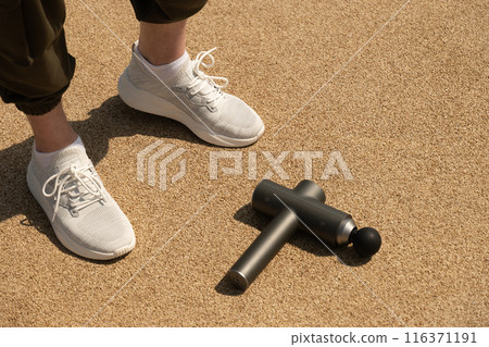 Athlete legs and percussion massager for warms up muscles in leg with an impact massager on outdoor sports area. Concept. Athlete legs and percussion massager for warms up muscles in leg with an impact massager on outdoor sports area. Concept. 116371191