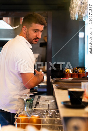 Waiter in white polo shirt working behind the bar in a restaurant. Vertical 116371287