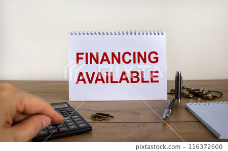 White note with inscription 'financing available' on beautiful wooden table, male hand on calculator, pen, paper clips, coins. Business concept. White background. 116372600