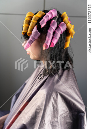 A woman in a salon cape with her hair in pink and yellow curlers 116372715