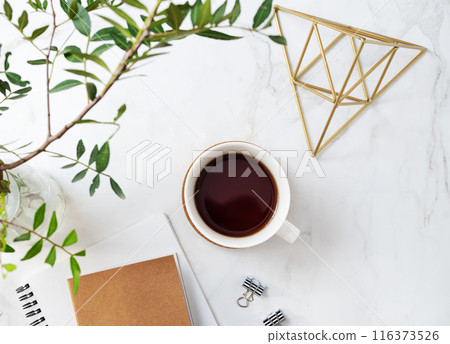 A cup of tea, craft notepad and accessories on a light marble background with green branches  116373526