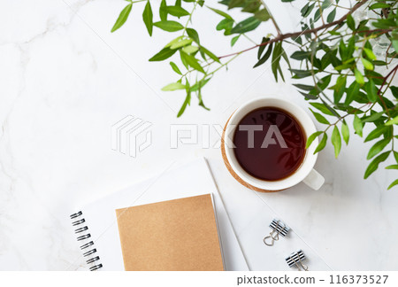A cup of tea and craft notepad on a light marble background with green branches close-up A cup of tea and craft notepad on a light marble background with green branches close-up 116373527