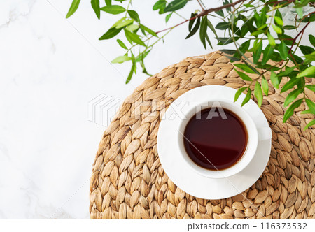 A cup of tea on a light marble background with green branches close-up. Spring women's concept. A cup of tea on a light marble background with green branches close-up. Spring women's concept. 116373532