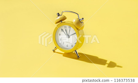 One small alarm clock with a double bell made of yellow metal on a yellow background with shadow.  116373538