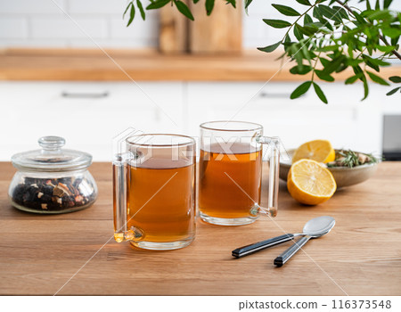 Two cups of tea with lemon and dry herbal flowers on a wooden countertop against the background  116373548