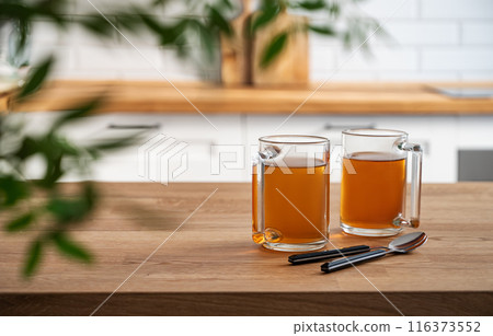 Two cups of tea  and brunch leaf close up on a wooden countertop against the background  116373552