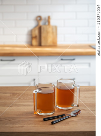 Two cups of tea  on a wooden countertop against the background of a white kitchen  116373554