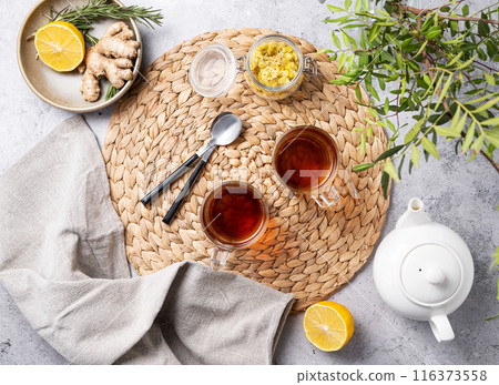Two cups of tea with lemon, ginger, teapot and dry herbal flowers on a marble background   116373558