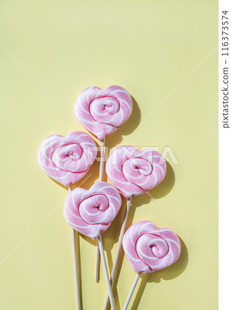 Pink lollipops in the shape of hearts on a yellow background. Top view and copy space Pink lollipops in the shape of hearts on a yellow background. Top view and copy space 116373574