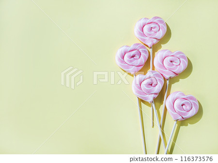 Pink lollipops in the shape of hearts on a yellow background. Top view and copy   space 116373576