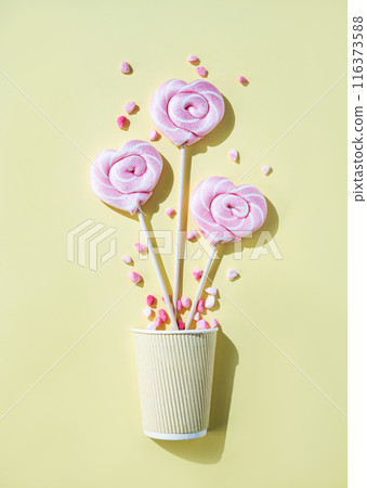 Pink lollipops in the shape of hearts at  paper cup with color sugar on a yellow background.  116373588