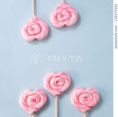 Pink lollipops in the shape of hearts on a blue background. Top view and copy   space 116373592