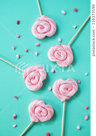 Pink lollipops in the shape of hearts with color sugar on a green background. Pink lollipops in the shape of hearts with color sugar on a green background. 116373599