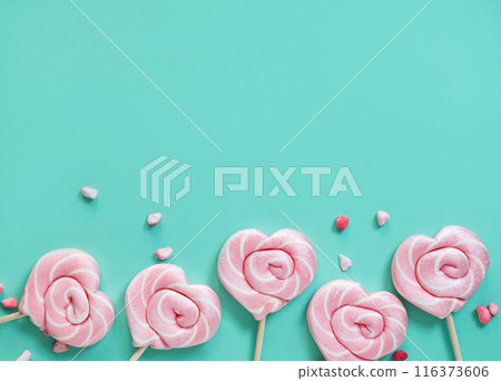 Pink lollipops in the shape of hearts with color sugar on a green background. Top view 116373606