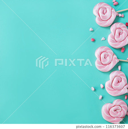 Pink lollipops in the shape of hearts with color sugar on a green background. Top view Pink lollipops in the shape of hearts with color sugar on a green background. Top view 116373607