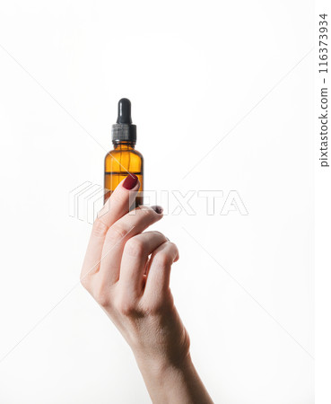 A woman's hand holds a bottle of cosmetics with serum for face and body on a white background. A woman's hand holds a bottle of cosmetics with serum for face and body on a white background. 116373934