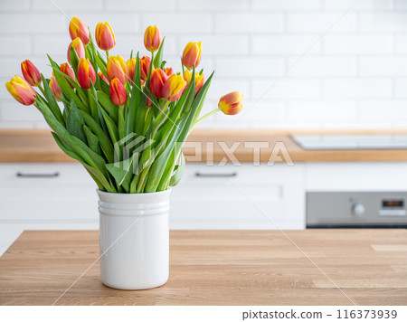 A beautiful bouquet of red and yellow tulips in a white vase on a wooden countertop  116373939