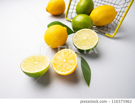 Fresh lemons and limes fall out of  a supermarket basket on a blue background. Citrus fruit concept 116373962