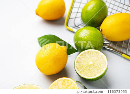 Fresh lemons and limes fall out of  a supermarket basket on a blue background close up. 116373963