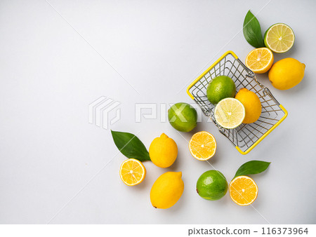 Fresh lemons and limes fall out of a supermarket basket on a blue background. Citrus fruit concept Fresh lemons and limes fall out of a supermarket basket on a blue background. Citrus fruit concept 116373964