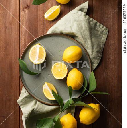 Fresh lemons with leaves in a green plate on a dark wooden background. Fresh lemons with leaves in a green plate on a dark wooden background. 116373989
