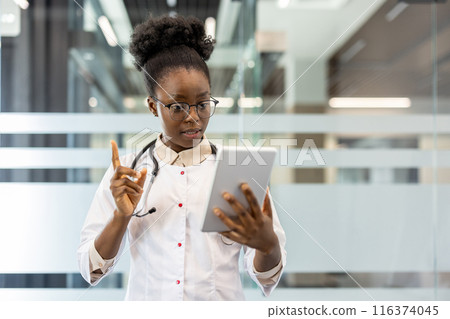 Female doctor wearing stethoscope using tablet for video call in modern office. Doctor making virtual consultation, communicating with patient. Professional healthcare worker using technology 116374045