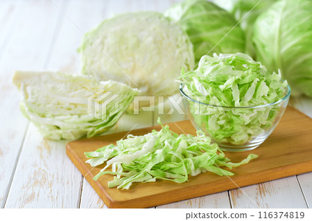 sliced fresh green cabbage in a clear glass bowl on a white wooden table. 116374819
