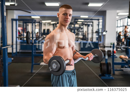 Portrait of a muscular bodybuilder lifts weights in a gym, showing off his biceps 116375025