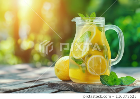 Lemonade with fresh lemon and mint in a jug on a wooden table outdoors. 116375525