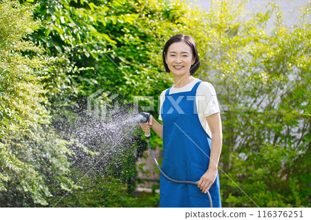 微笑的中年婦女在花園裡的綠樹澆水 116376251