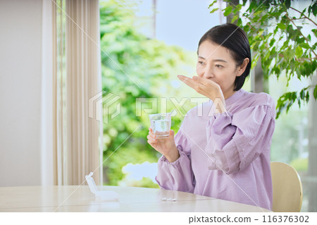 Smiling middle-aged woman taking medicine in the living room Smiling middle-aged woman taking medicine in the living room 116376302